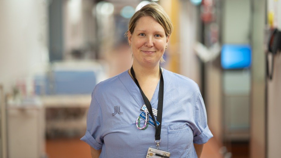 Avancerade specialistsjuksköterskan Andrea Lundin har det mellanblonda håret uppsatt i en tofs och bär sina blå arbetskläder.