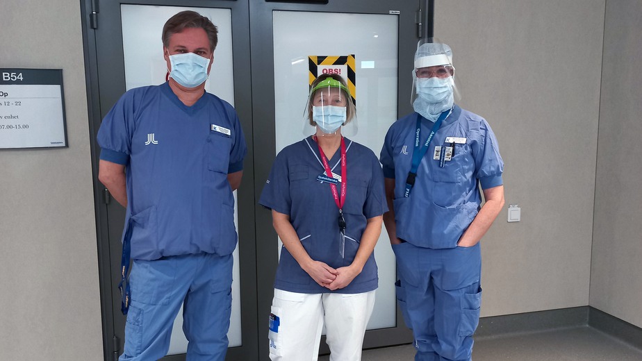 Tre vårdklädda personer med munskydd och visir.