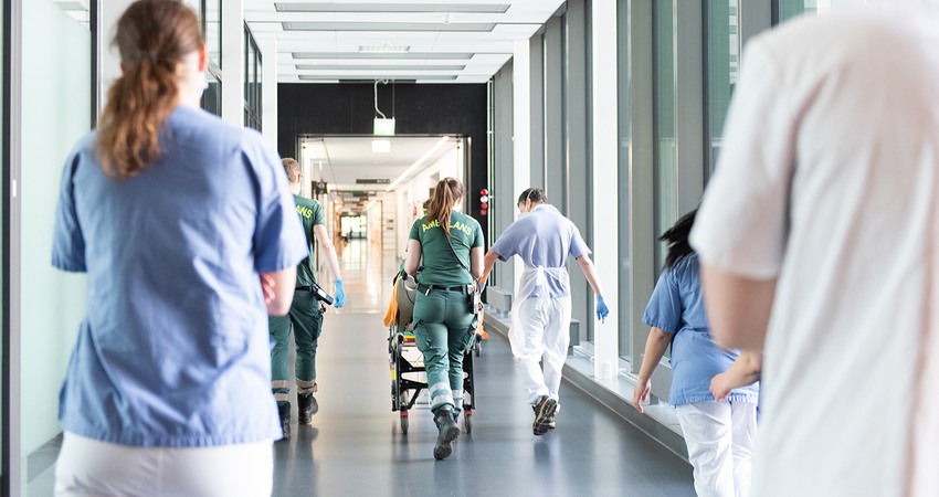 ambulanspersonal springer i en vårdkorridor med patient i säng
