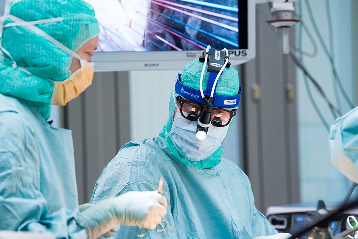 Två kirurger under operation varav den ena tittar in i kameran