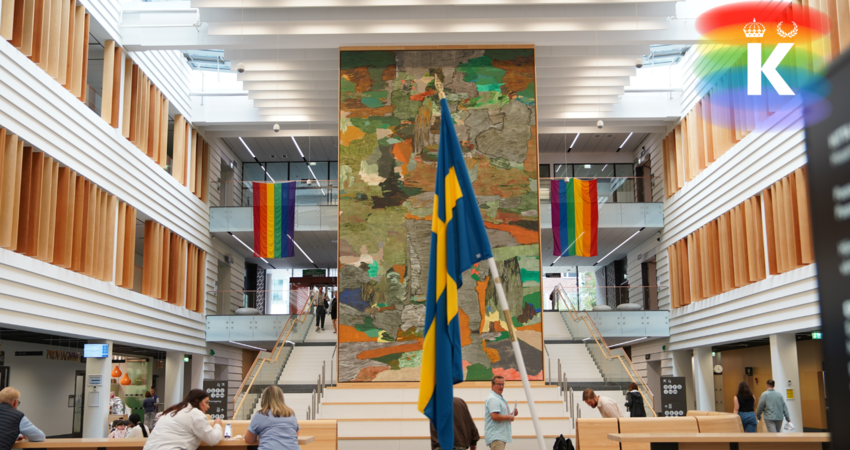 Två prideflaggor, i regnbågsfärger, hänger i huvudentrén vid Karolinska i Solna på vardera sida. Svenska flaggan syns i förgrunden.