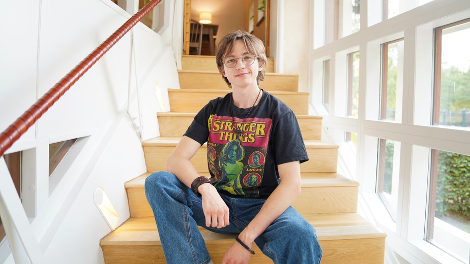 Gustav Weissinger har en svart Stranger Things- t-shirt och sitter på en träfärgad trappa i Ronald McDonald Hus.