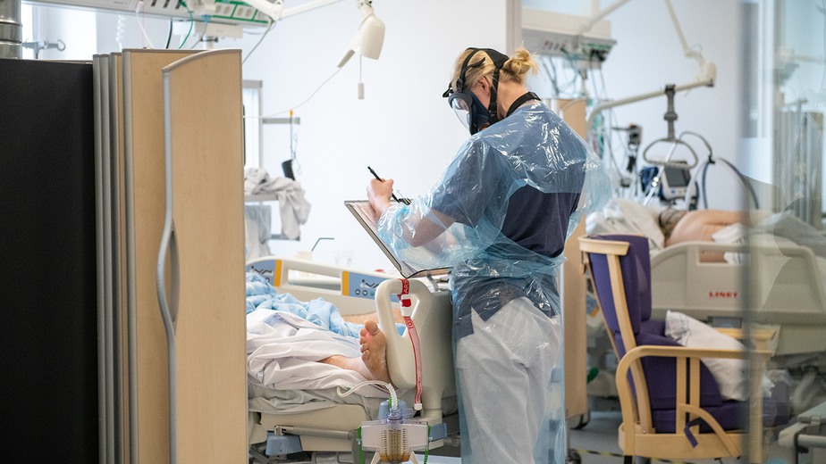 Medarbetare antecknar vid fotändan av patientsäng på MIMA i Huddinge. Patienterna har covid-19, medarbetaren skyddsdräkt.