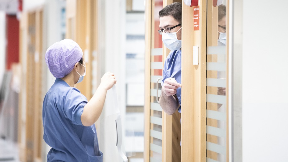 Två anställda i blå sjukhuskläder samtalar i en korridor.