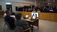 Tre kursledare sitter vid ett mindre bord och tittar ut över deltagarna i aulan.