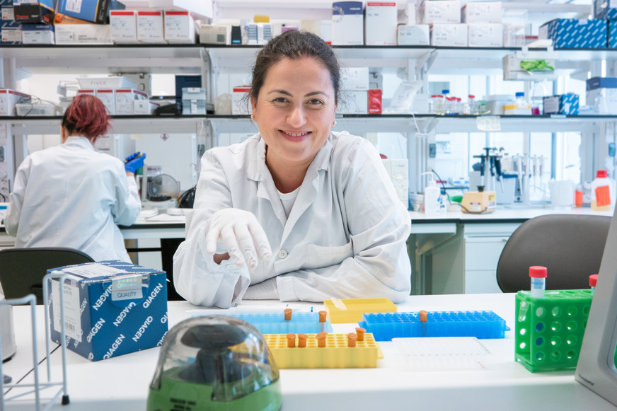 Kvinnlig forskare sitter vid labbänk med provrör framför sig