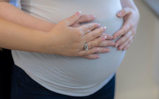 Gravid kvinnas mage med händer som håller om magen