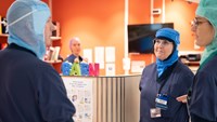 En man och två kvinnor i vårdkläder pratar med varandra inne på sjukhus.
