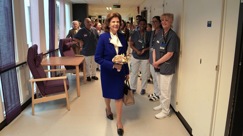 Drottning Silvia går i en korridor på vårdavdelningen omgiven av medarbetare.