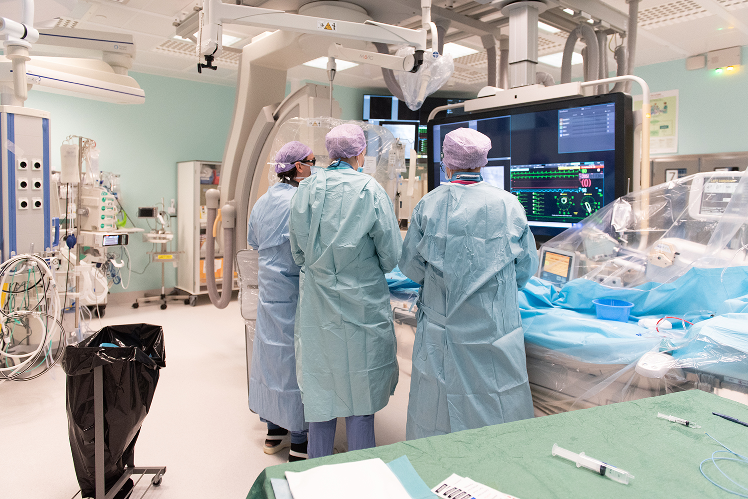 Tre läkare står i en operationssal med monitorer framför sig