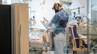 Medarbetare antecknar vid fotändan av patientsäng på MIMA i Huddinge. Patienterna har covid-19, medarbetaren skyddsdräkt.