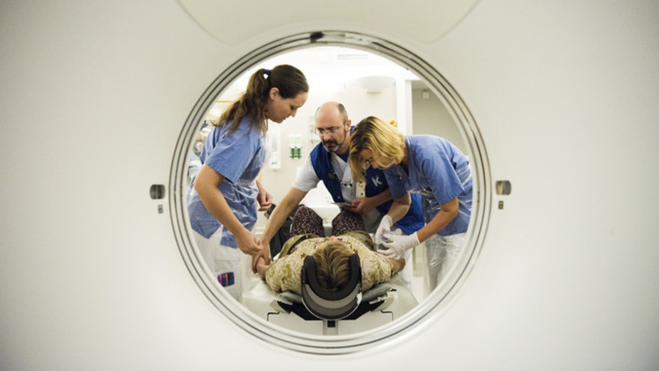 vårdpersonal står med patient som förs in i magnetkamera