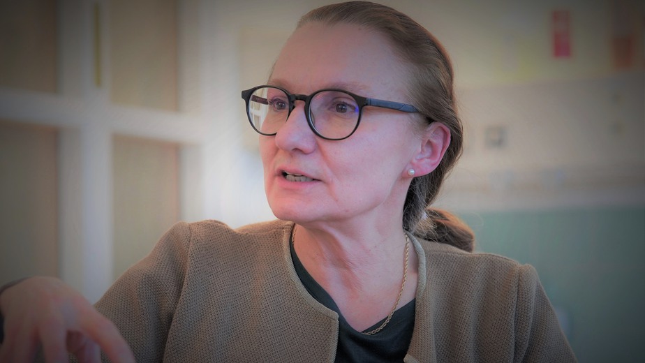 Svetlana Bajalica Lagercrantz sitter i brungröna kläder och glasögon och diskuterar i en kontorsmiljö