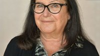 Judith har mörkt rakt hår till axlarna och svarta ovala glasögon.