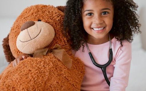 Stethoscope, teddy bear and girl with a child her stuffed animal with a smile in her house. Portrait of happy female kid holding a fluffy toy, learning to be a doctor or pediatrician in healthcare.