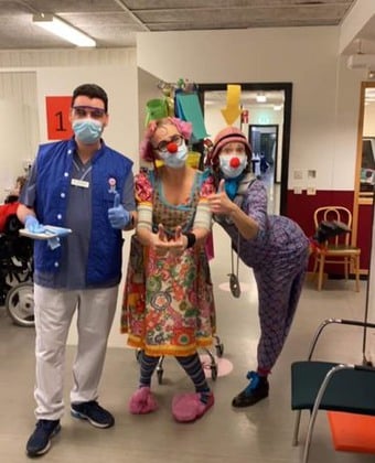 Clownerna från Clownmedicin hälsar på vaccinationsmottagningen i Huddinge och står med en vårdklädd medarbetare.