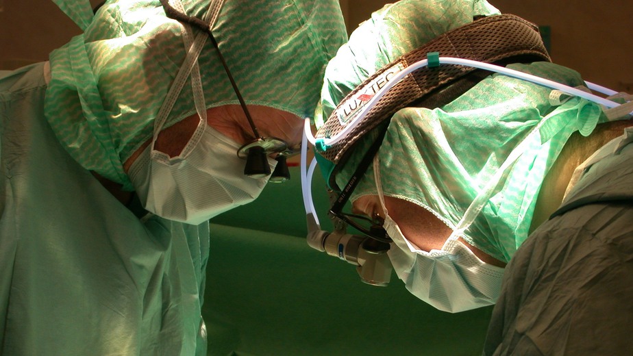 Två kirurger i gröna operationsmössor tittar ner på patient