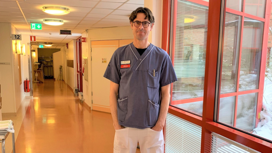 Överläkare Ola Blennow i blåvita arbetskläder står i en sjukhuskorridor.