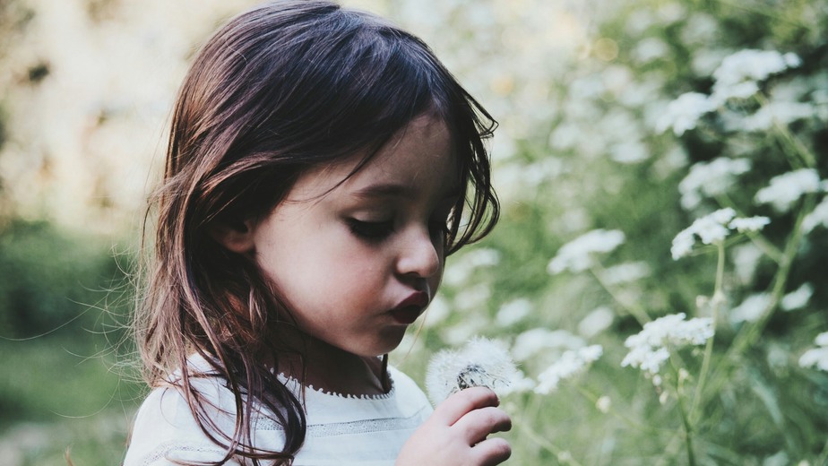Mörkhårig liten flicka i grönska och omgiven av vita blommor.