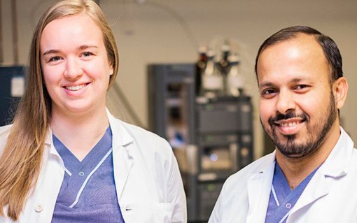 Två vårdklädda medarbetare tilttar in i kameran på ett laboratorieum
