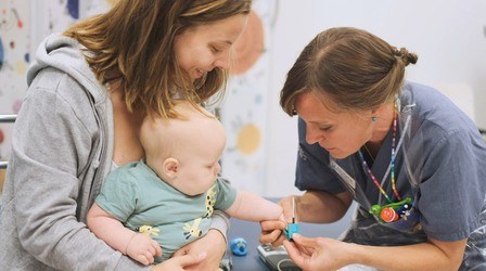 Mamma och nyfiken bebis med vårdklädd personal