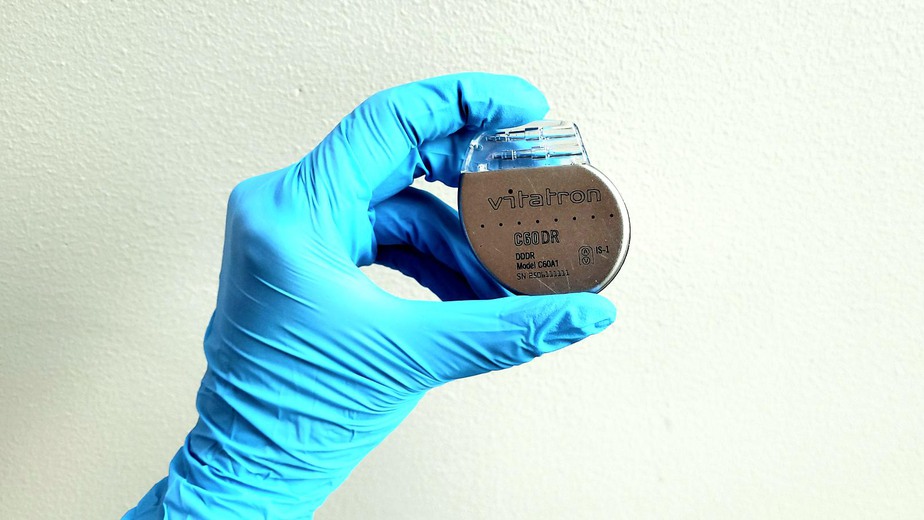 En hand med blå handske som håller i en pacemaker