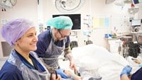 Cechael står intill en kvinna på en operationsbädd.