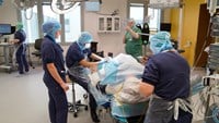 Cechael står vid en sjukhusbädd i en operationssal. I bädden ligegr en patient med ett fult bensår.