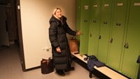 Cechael står i svart lång vadderad jacka och öppnar ett grönt omklädningsskåp.