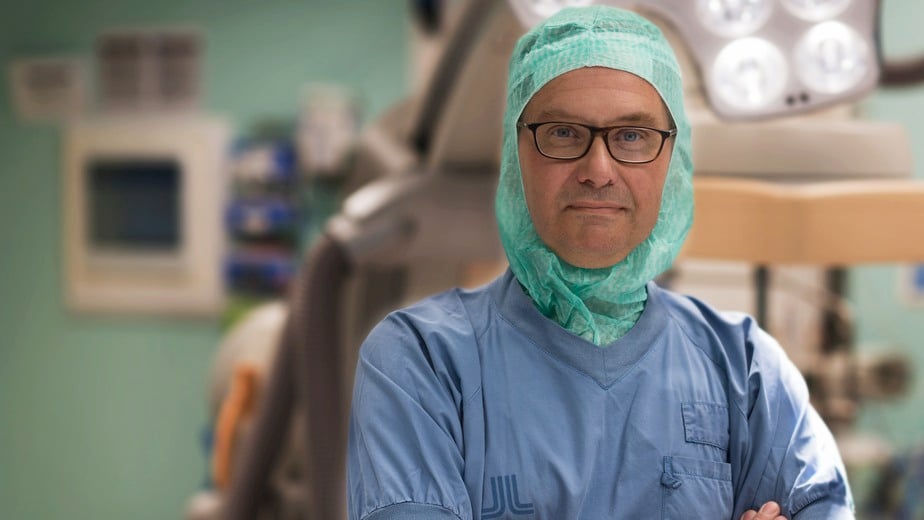 Fredrik Galder bär blå sjukhuskläder och en grön operationsmössa.