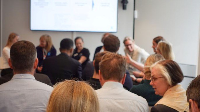 Bilden visar personer från vård och företag som diskuterar i en konferenssal.