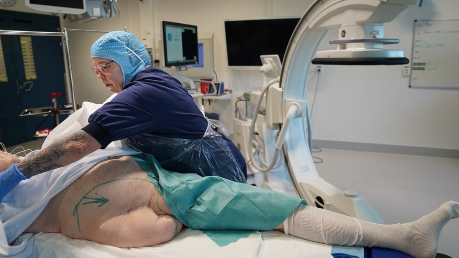En sjuksköterska pysslar om en manlig patient i en sjukhusbädd.
