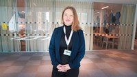 Kvinna med rött hår och blå kavaj står framför en glasvägg.