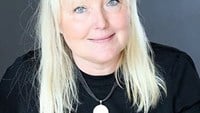 Ann har blont långt hår och bär en svart långärmad tröja.
