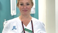 En kvinna i vit sjukhusklädsel står i ett rum.