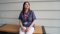 Kvinna i sjukhusets blå arbetskläder sitter p´å en bänk.
