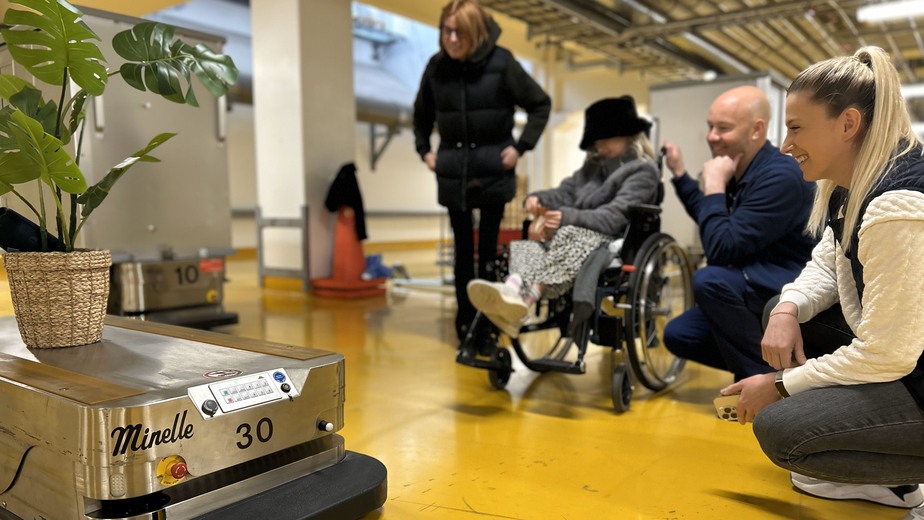 En grupp människor i ett rum med en robot och en växt.