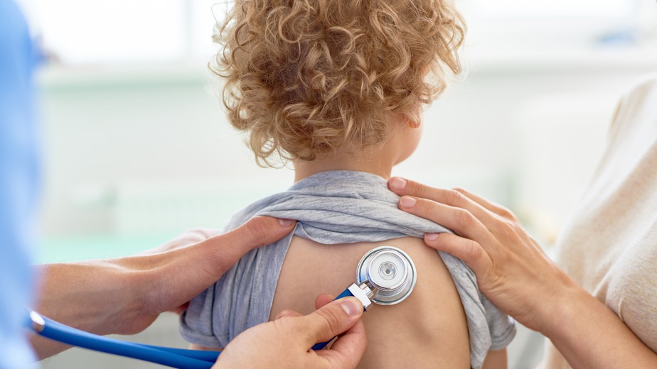 Liten blond lockhårig pojke undersöks med ett stetoskop på ryggen.