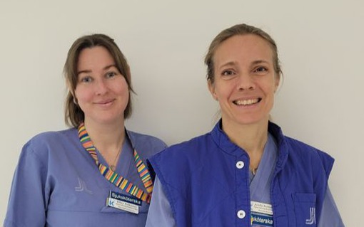 Ellen Eriksson och Arielle Reitberger i vårdkläder står bredvid varandra framför en vit vägg