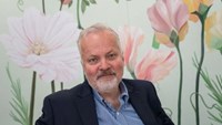 Man i svart kostym och blå skjorta sitter i en fåtölj.