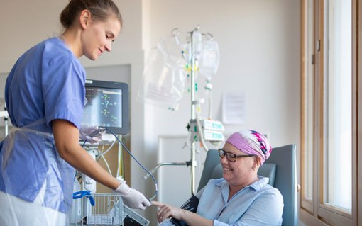 Cancersjuk kvinna med rosa sjal på huvudet blir  undersökt av en kvinnlig sjukhusanställd
