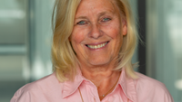 Angelica står i rosa kläder i  och blå jeans leendes i Karolinska i Solnas korridor.