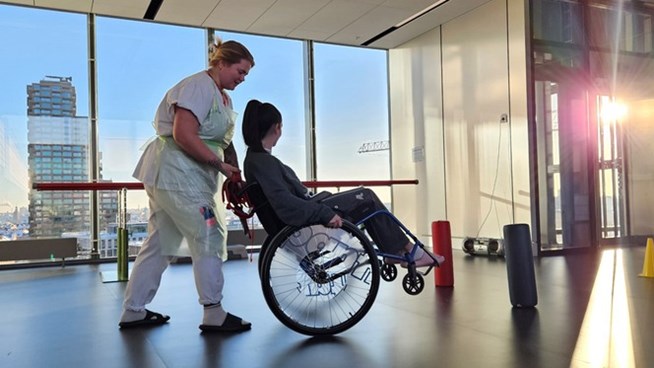 Sjuksköterska som kör patient i rullstol i korridor