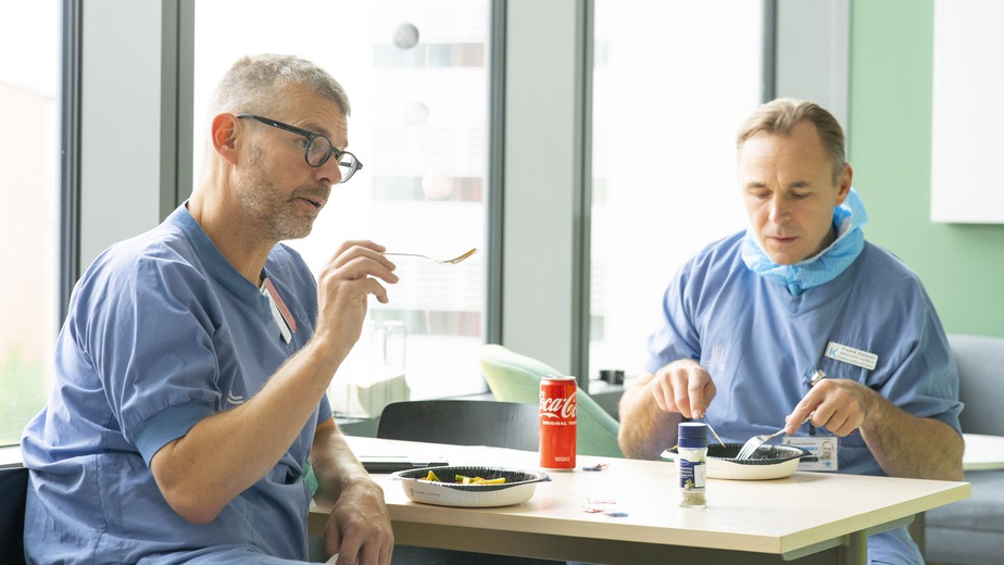 Läkarna Robert Bränström och Fredrik Karlsson sitter vid ett bord i lunchrummet och äter varsin färdigrätt.