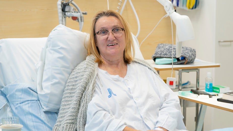 Patienten Eva Nygren ligger i sjukhussängen och vilar iklädd region stockholms vita patientkläder