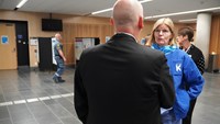 Kvinna i blont hår, glasögon och blå sjukhuskläder samtalar med sjukhusdirektören.