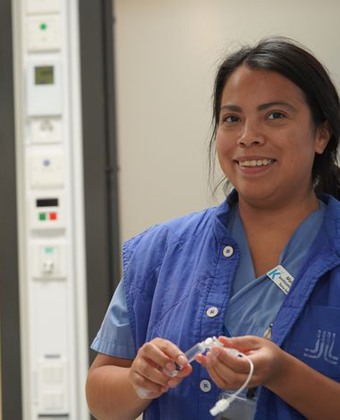 Specialistsjuksköterska Malee Dekker i blå arbetskläder ler brett mot kameran.