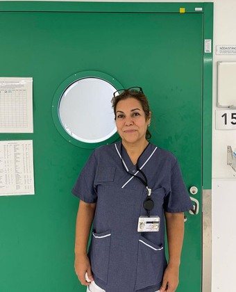 Koordinatorn Nasrin Tajfar i blå arbetskläder står framför en grön dörr i sjukhuskorridoren