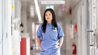 Mary Grace Sabado har svart långt hår och blå sjukhuskläder. Hon står mitt i en korridor på en vårdavdelning,