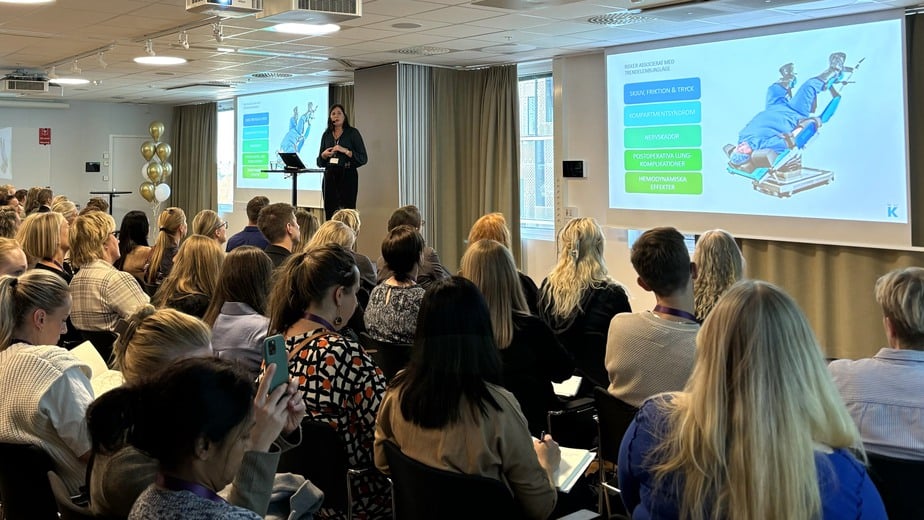 En fullsatt föreläsningssal med människor som tittar på en bild som visar en patient i bakåtlutat läge på en brits.